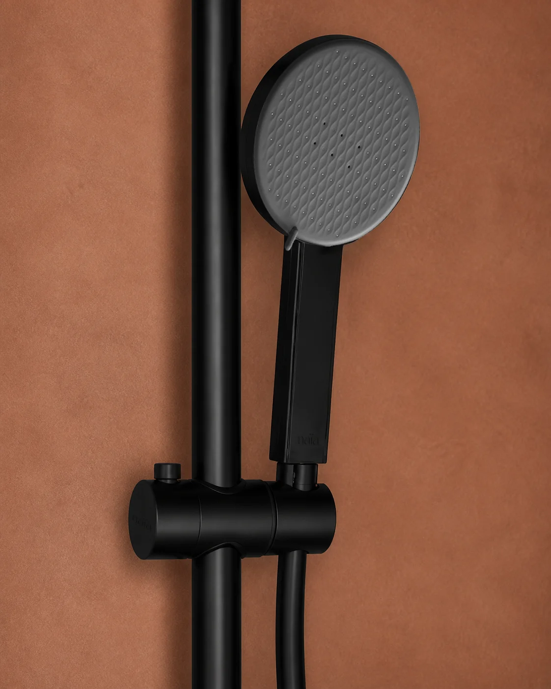 Close-up of the matte black Dana hand shower in its holder on a terracotta wall