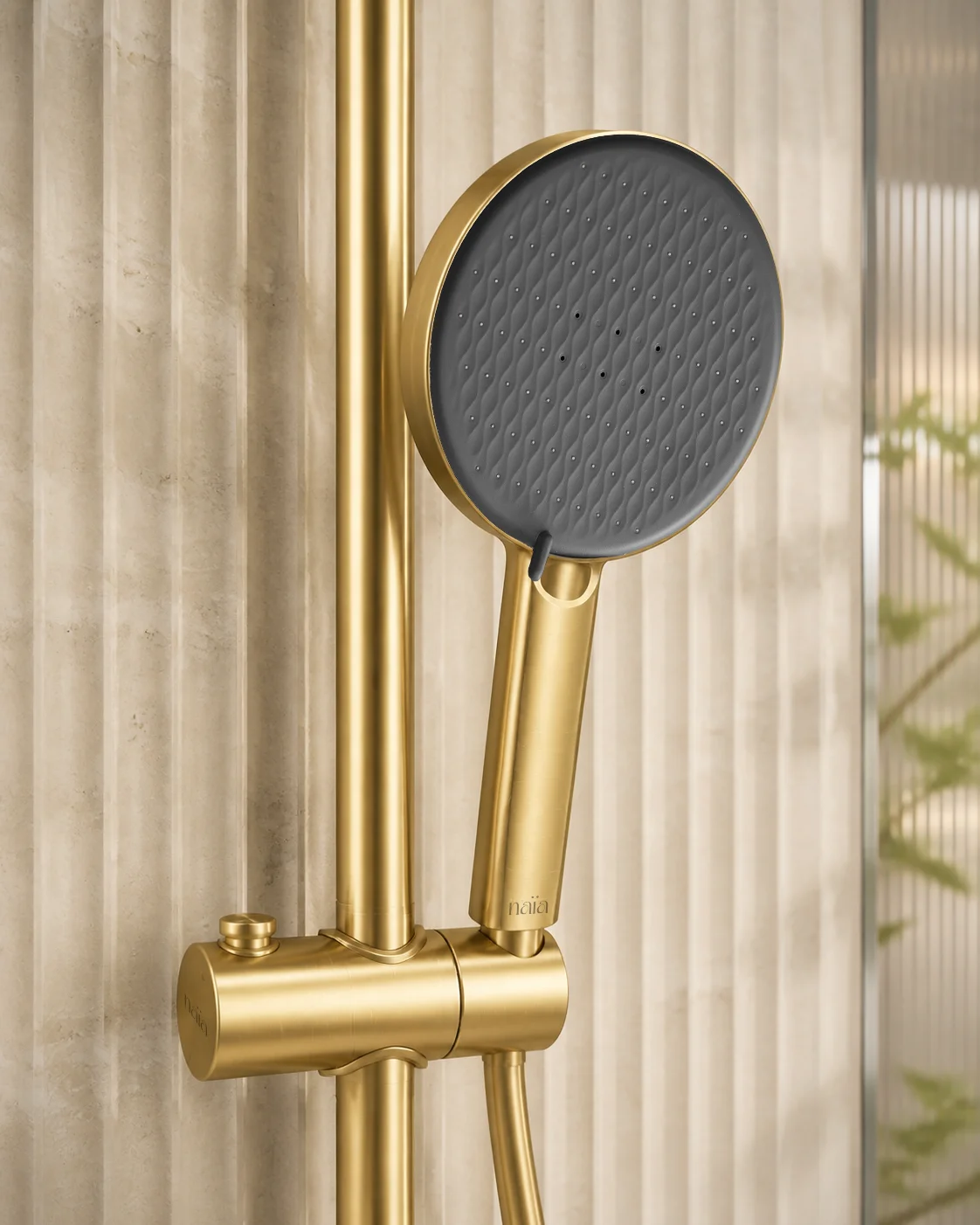 Brushed gold Rima hand shower in its sliding holder against fluted travertine