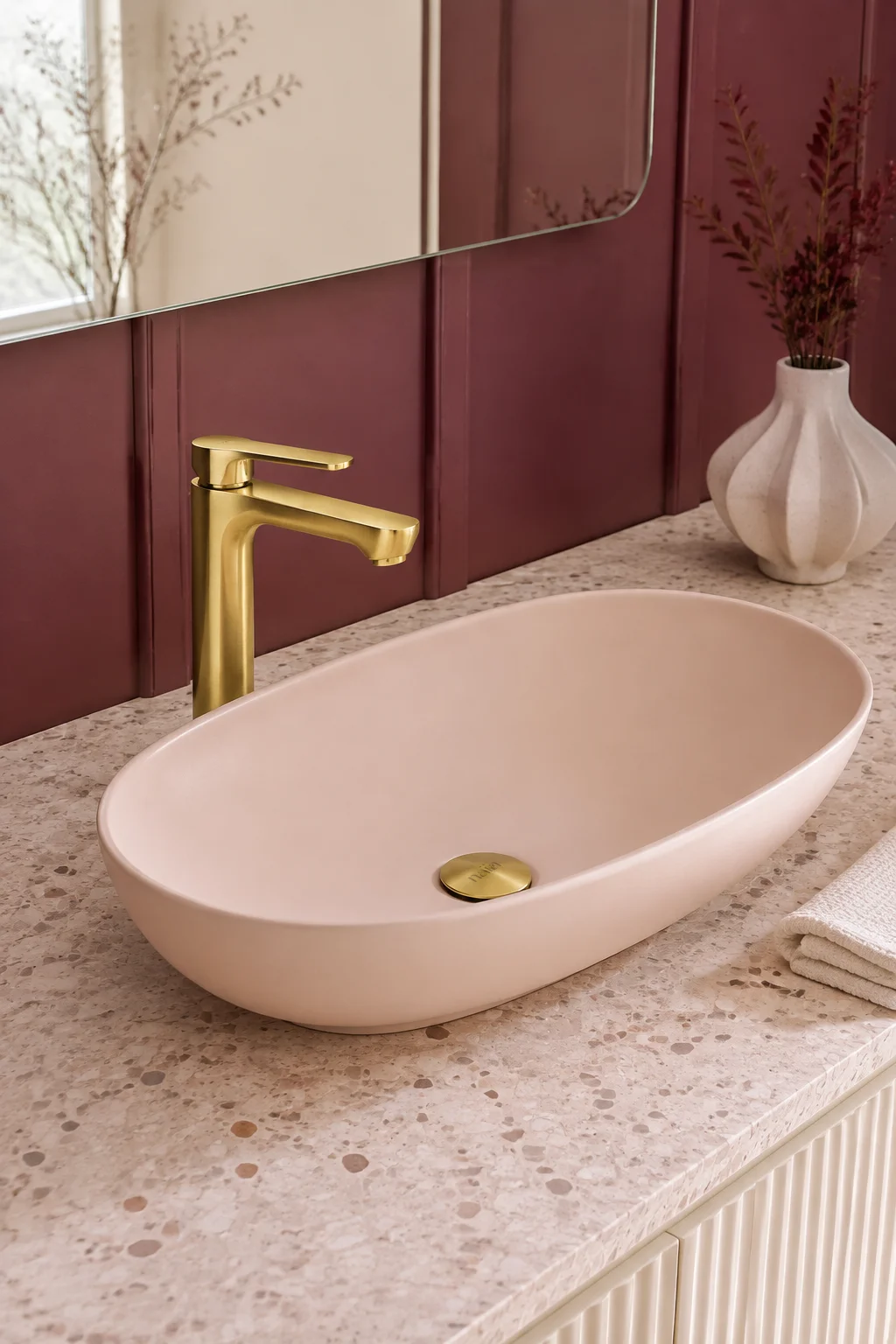 Brushed gold Tala mixer with a blush oval basin against burgundy panelling