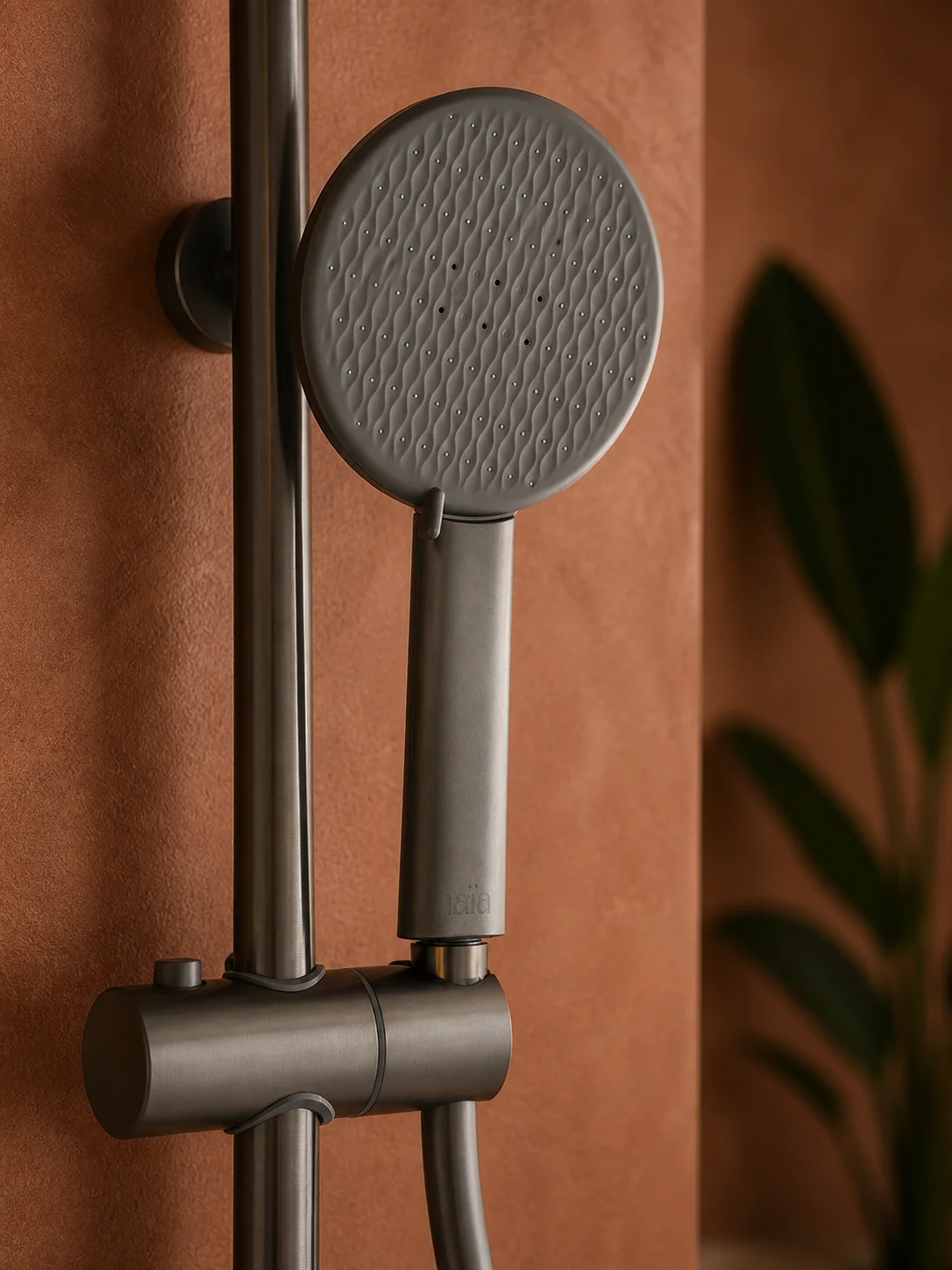 Close-up of the gun grey Rima hand shower in its holder on a terracotta wall